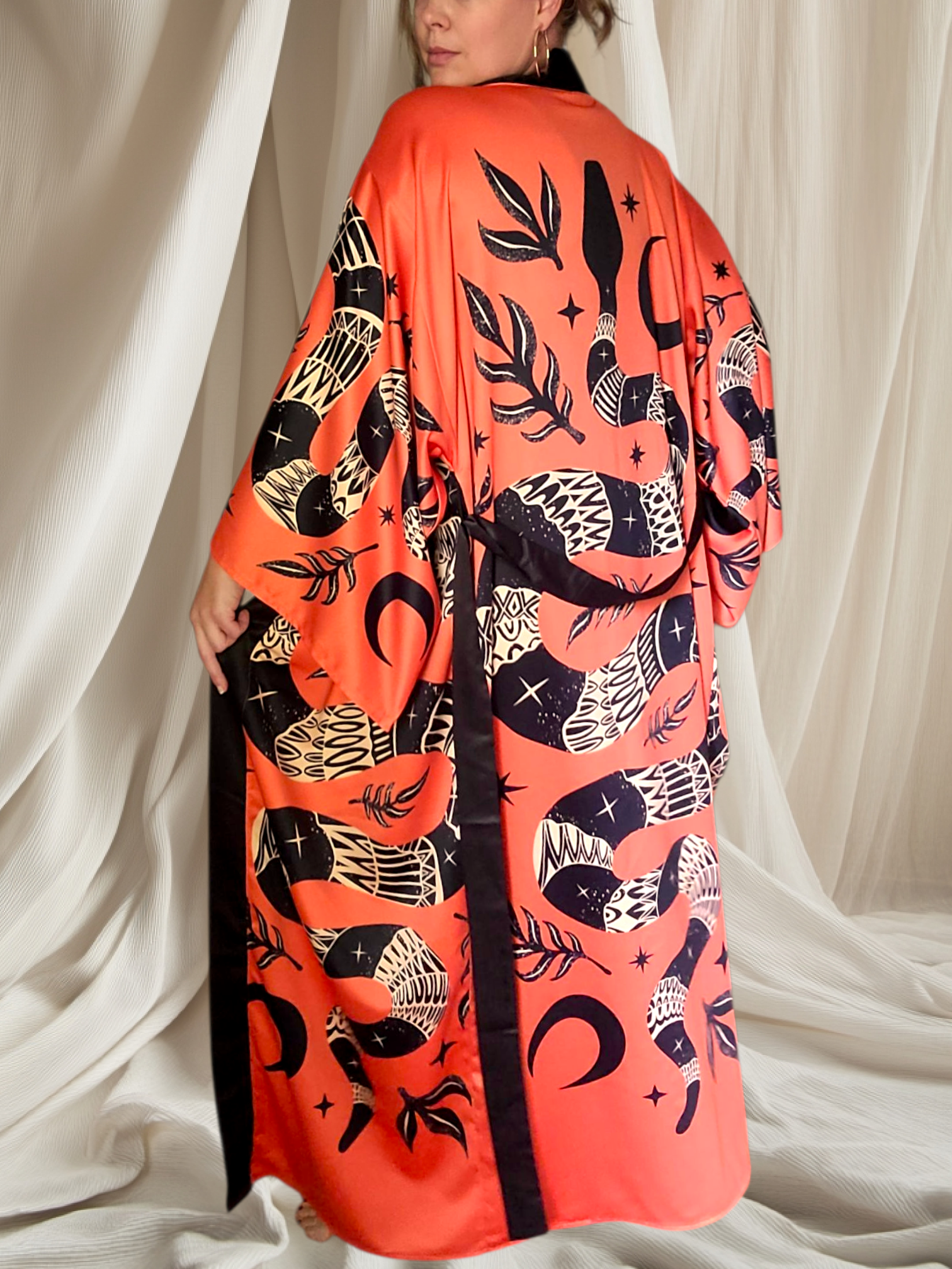 Person wearing an orange kimono with black and white pattern against a white curtain background