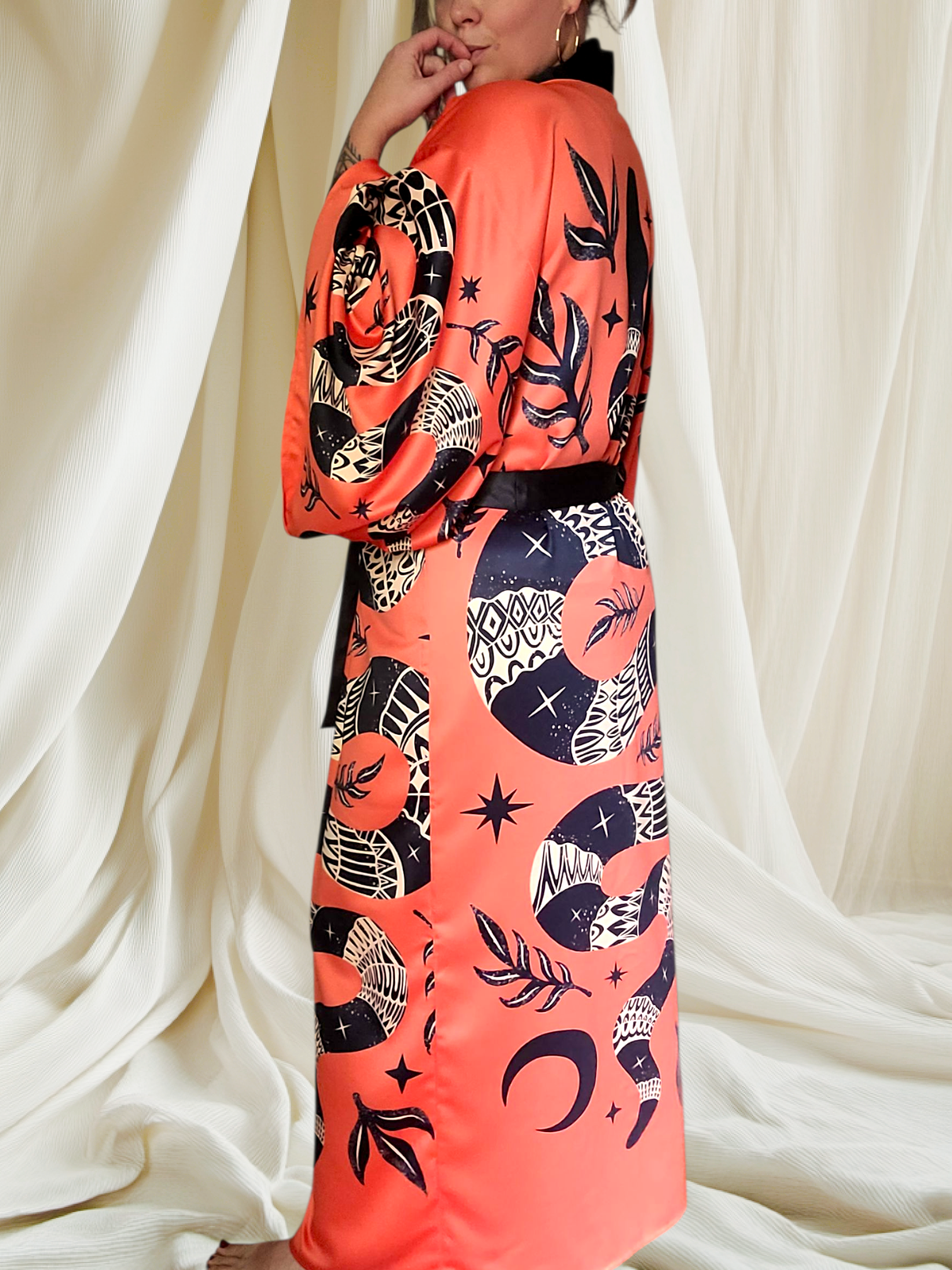 Person wearing a vibrant orange kimono with black and white patterns against a white curtain background
