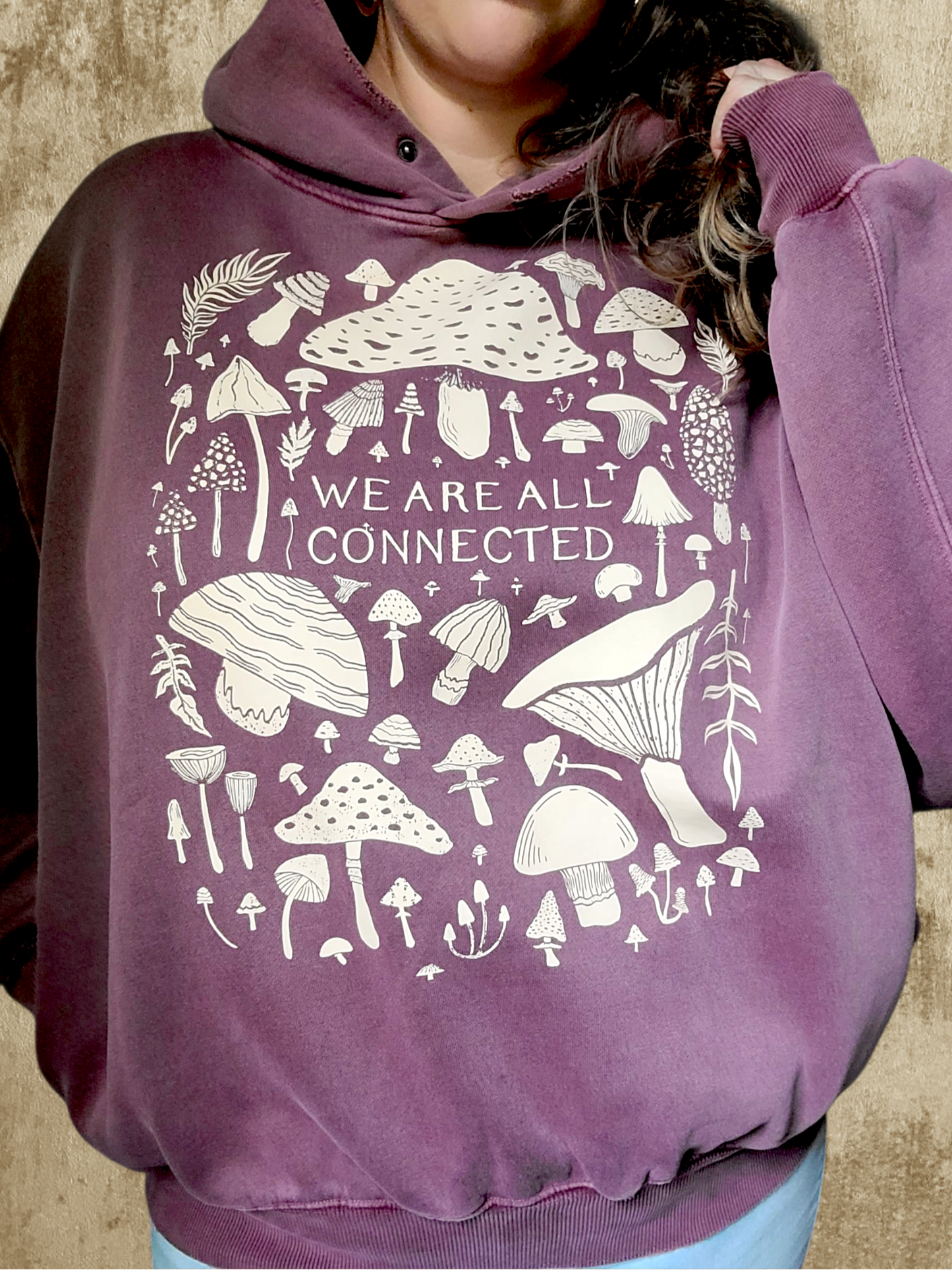 Purple hoodie with mushroom design and 'We Are All Connected' text on a textured background