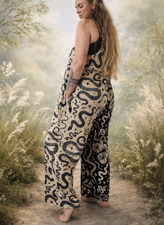 Woman wearing a snake-patterned color block loose jumpsuit stnding in a natural setting with trees and flowers