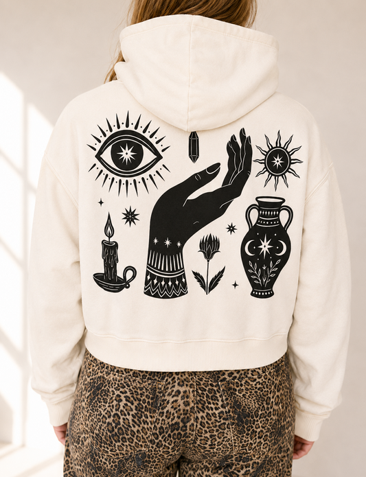 A person viewed from behind wearing an off-white cropped hoodie with a large black occult-style graphic print on the back, paired with leopard-print pants.