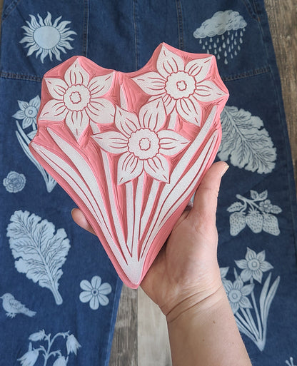 Hand holding a pink floral-patterned block print against a blue fabric background with floral designs.