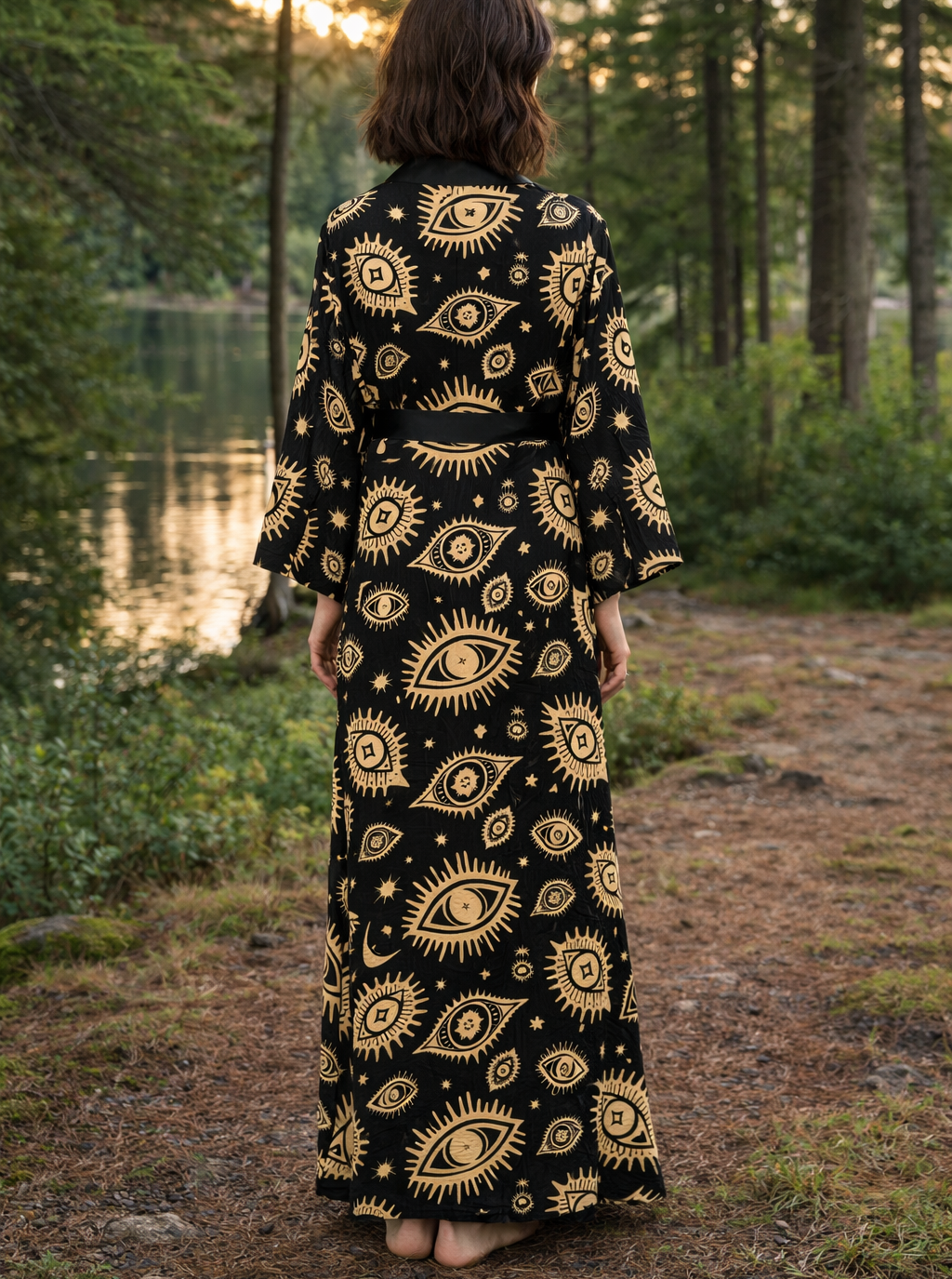 Person wearing a black kimono robe dress with gold eye patterns in a forest setting