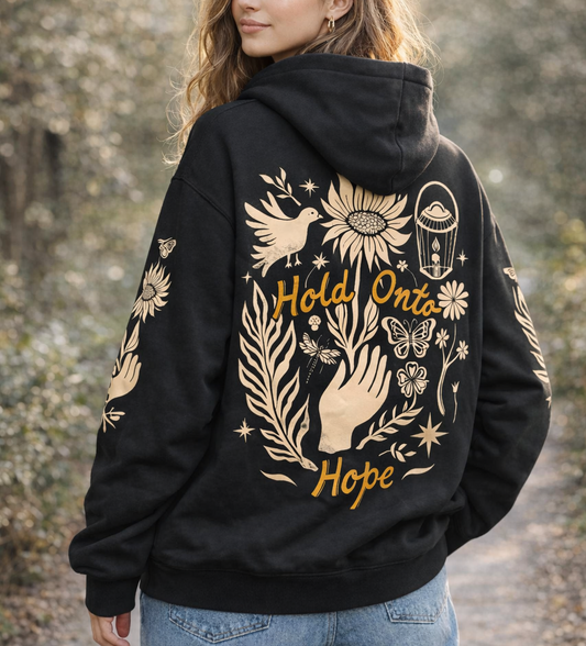 Person wearing a black hoodie with gold designs and text outdoors