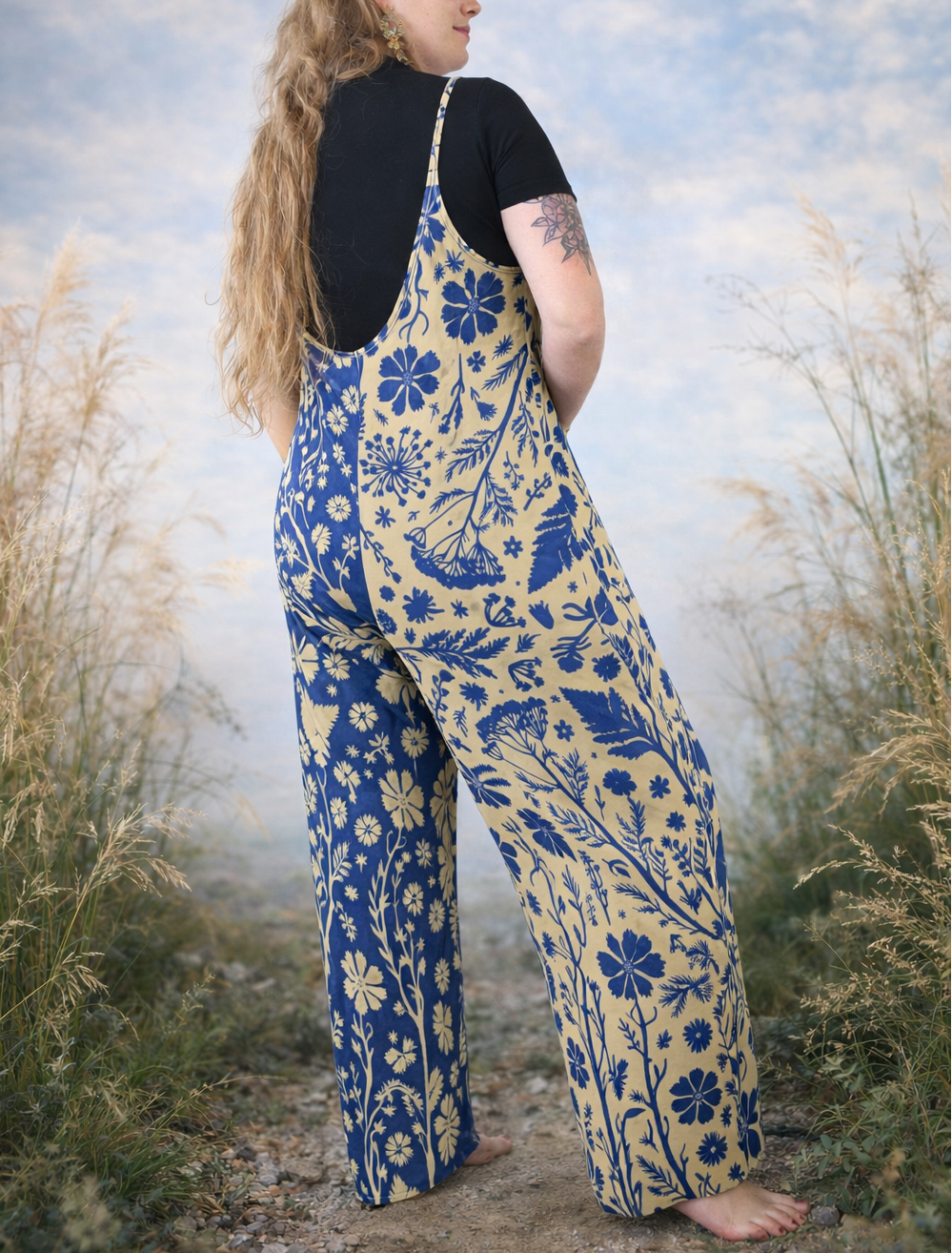 Person wearing a blue and yellow floral patterned jumpsuit standing in a natural setting with tall grass and a cloudy sky.