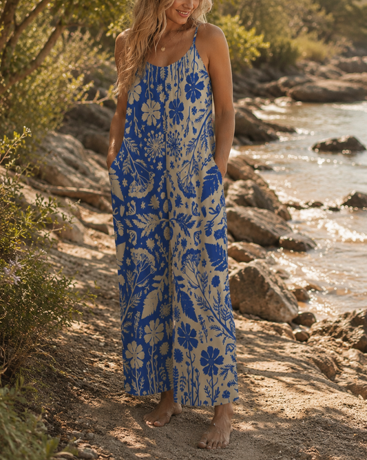 Woman in a blue floral dress standing on a rocky path by the water.