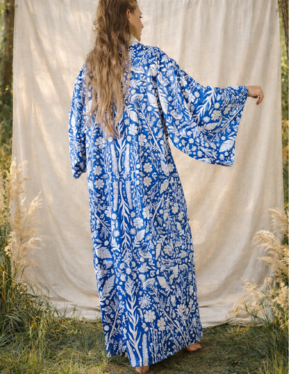 Woman wearing a blue floral kimono standing in front of a white curtain in a forest setting.