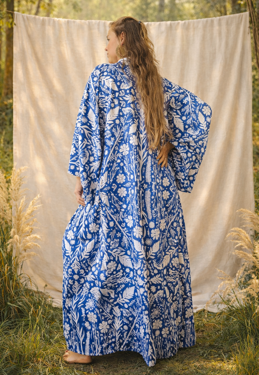 Woman wearing a blue floral kimono robe dress standing in a natural setting with a white curtain.