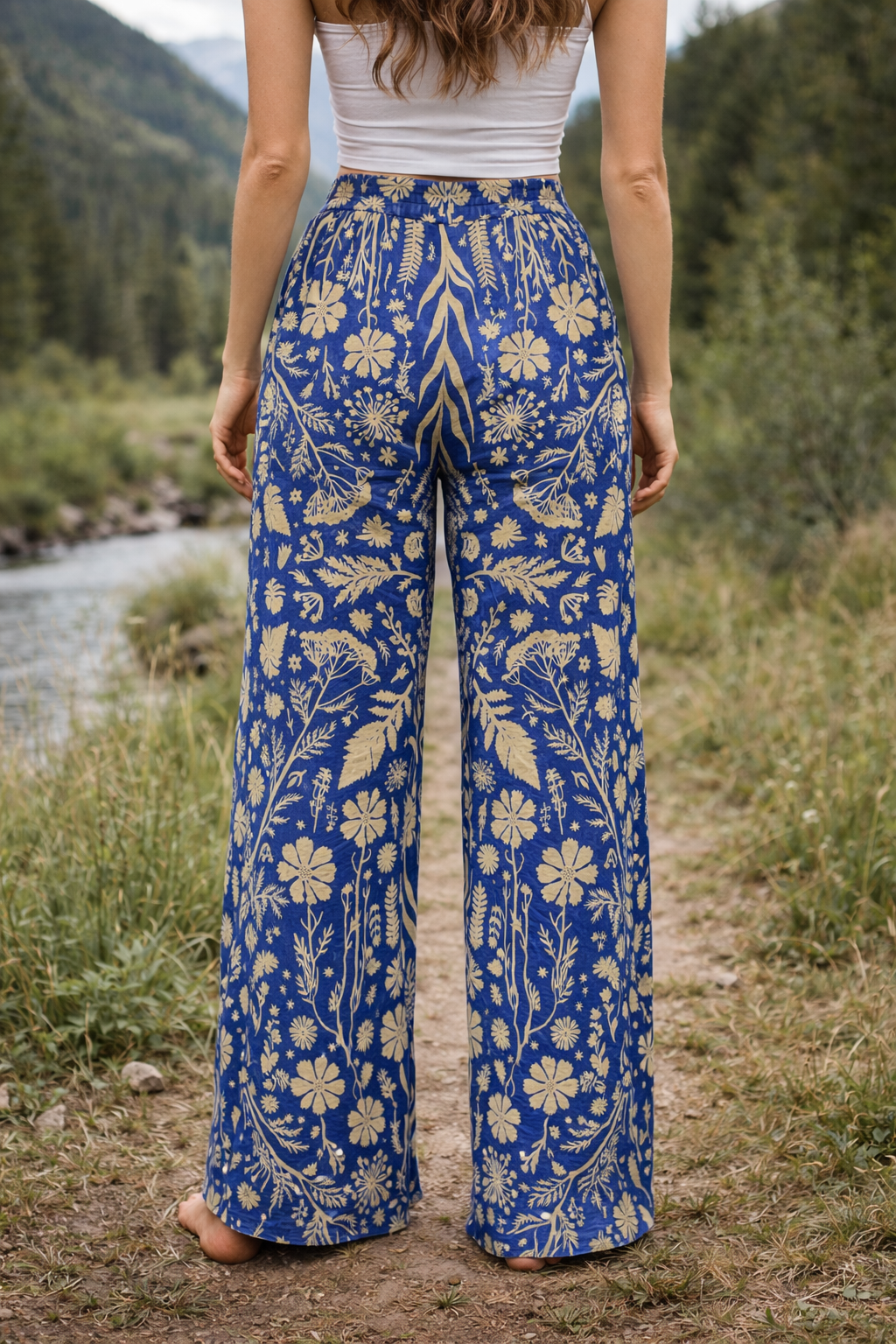 Person wearing blue floral-patterned pants standing in a natural setting with trees and a stream.