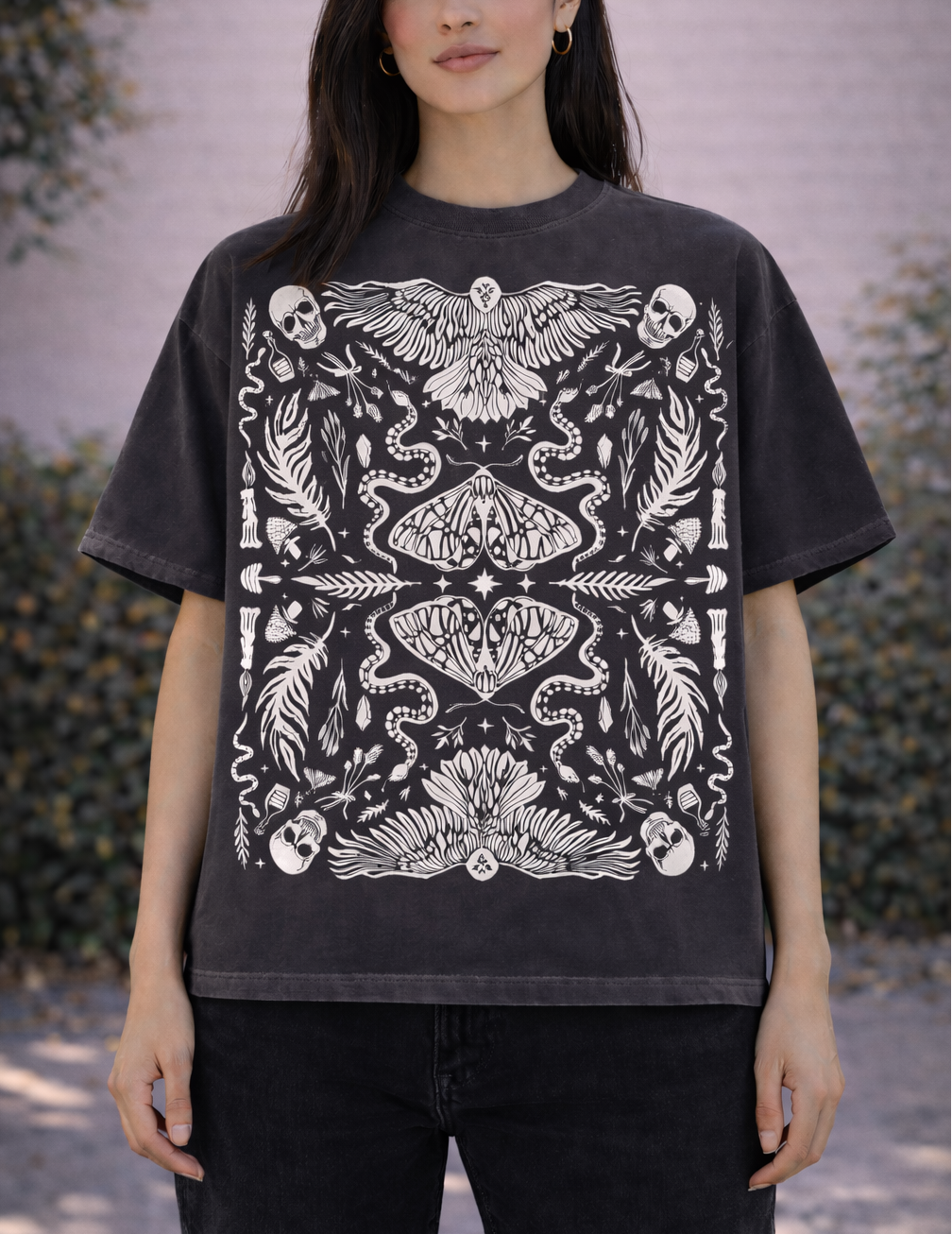 Person wearing a black t-shirt with white intricate witchy botanical design outdoors.