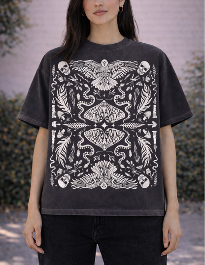 Person wearing a black t-shirt with white intricate witchy botanical design outdoors.