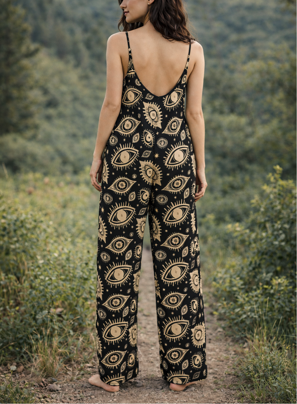 Woman wearing a black and gold patterned jumpsuit standing in a natural setting with greenery.