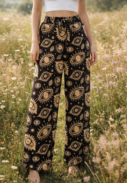 Person wearing black high waist lounge pants with gold eye patterns in a field