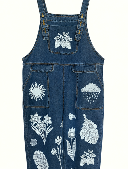 Blue denim overalls with white floral and nature-themed embroidery on a white background