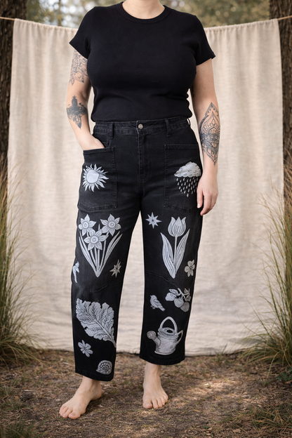 Person wearing black t-shirt and black pants with white floral patterns standing against a natural background.