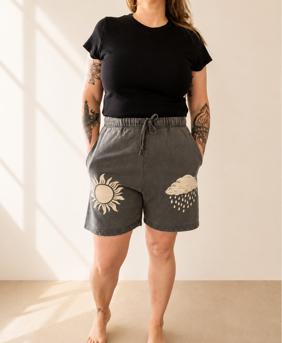 Person wearing black t-shirt and gray shorts with sun and cloud designs on a beige background