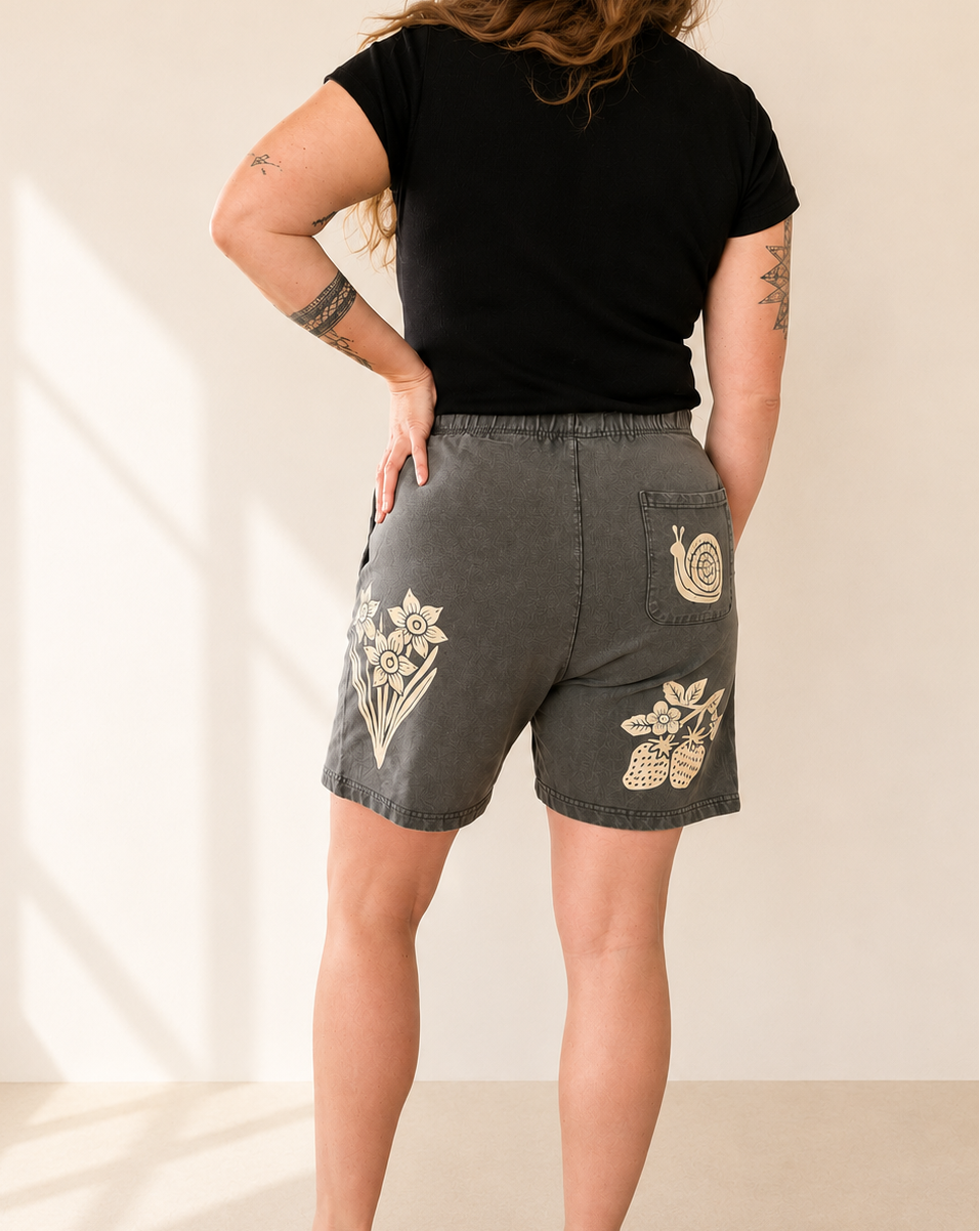 Person wearing black shorts with floral embroidery on a beige background