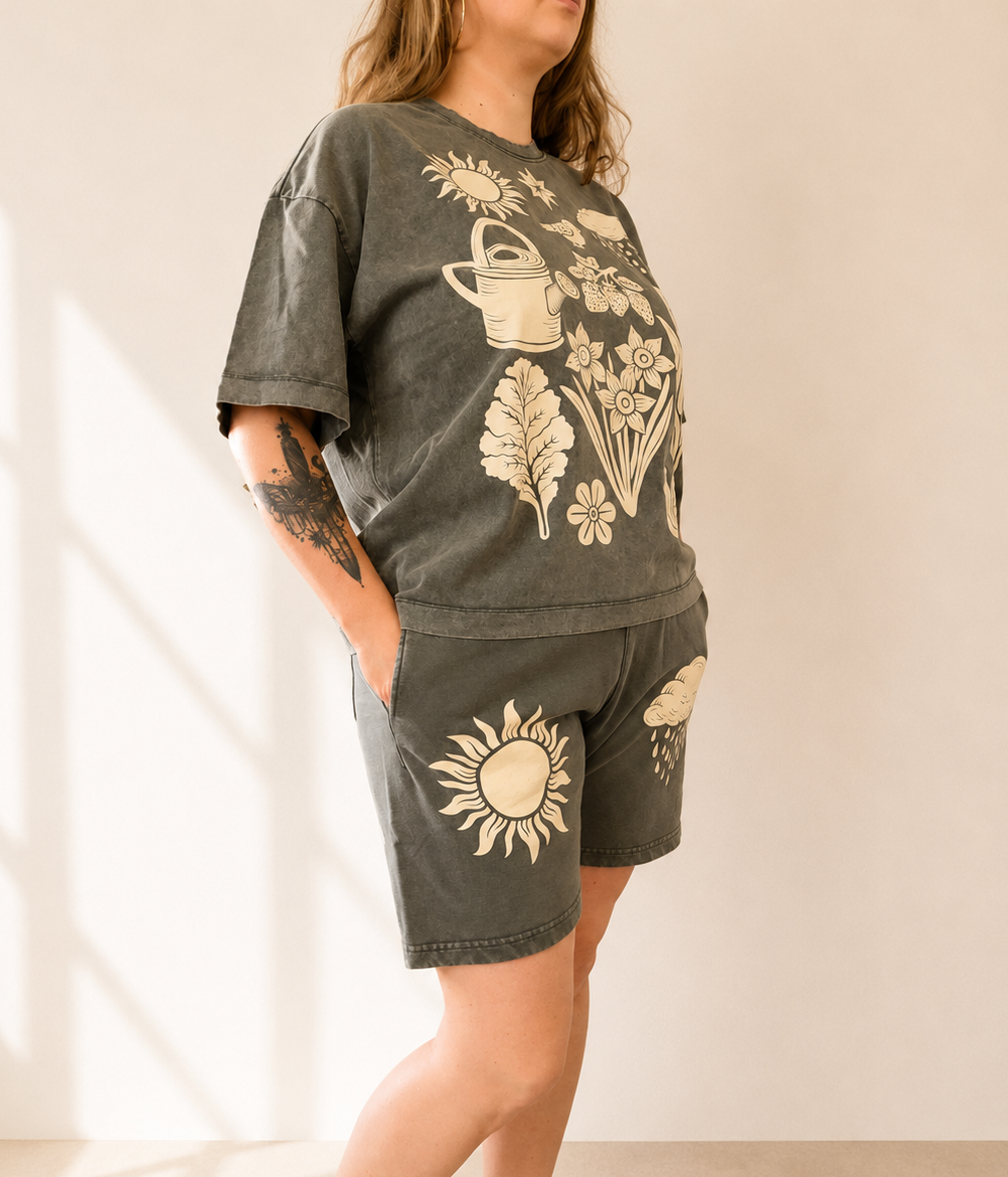 Person wearing a dark gray t-shirt and shorts with floral and sun designs on a neutral background