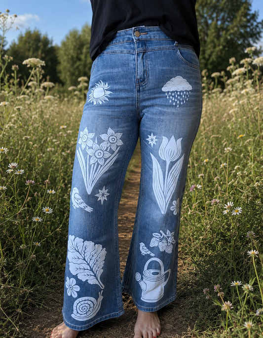 Person wearing blue jeans with white floral and nature-themed designs standing in a field.