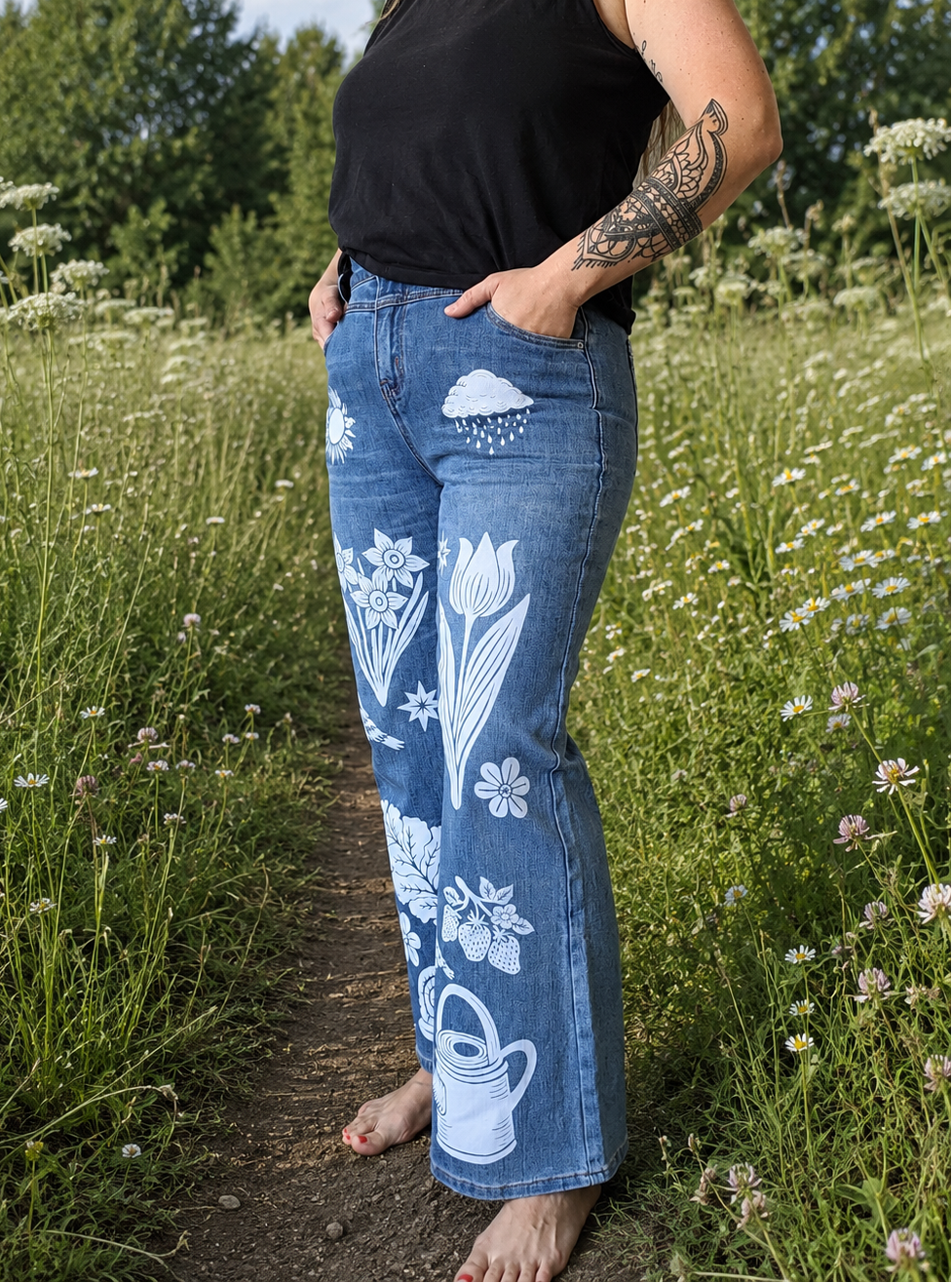 Person wearing blue jeans with white floral designs standing in a field of wildflowers.
