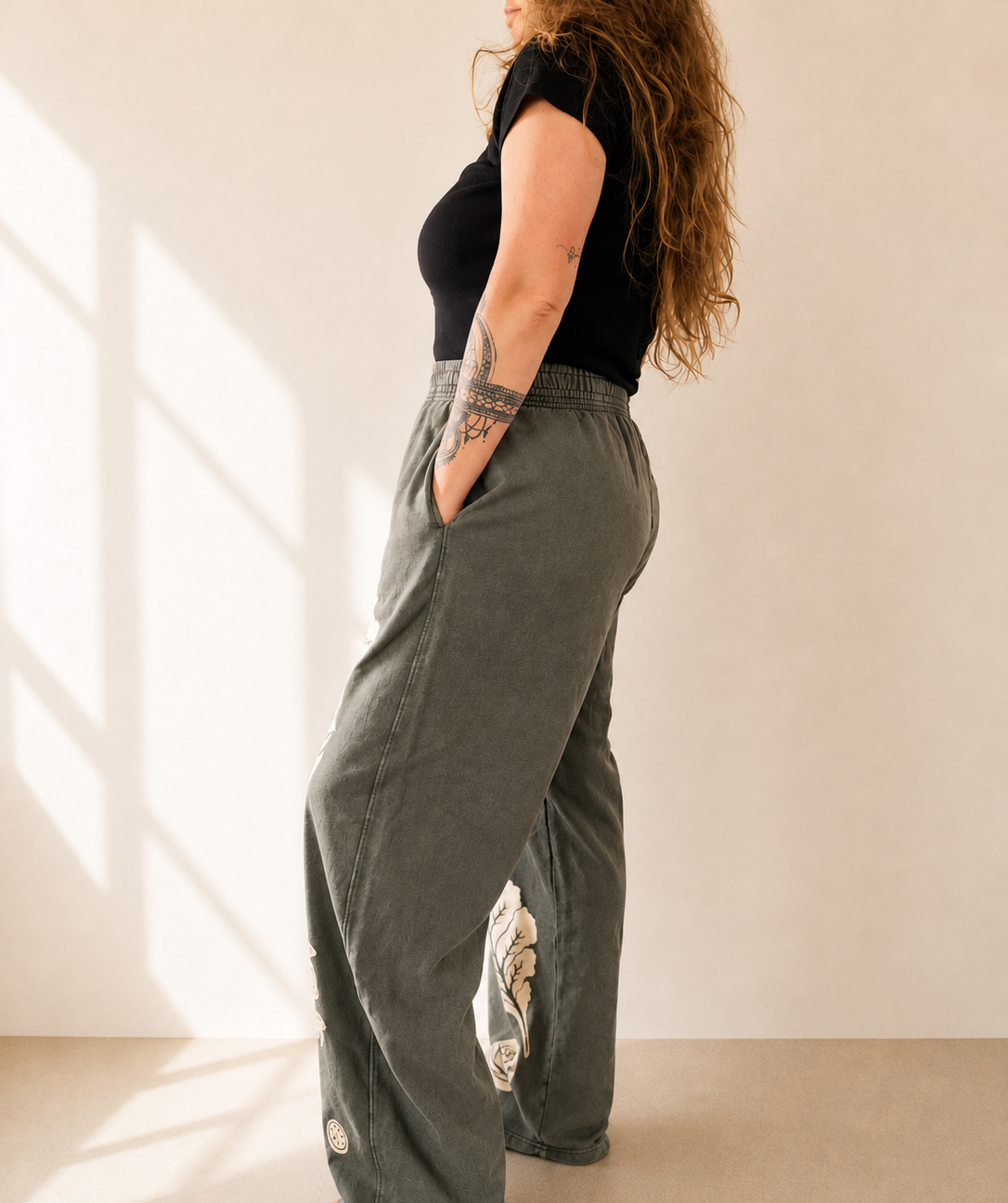 Person wearing a black top and green wide-leg pants with a beige background