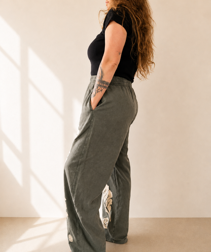 Person wearing a black top and green wide-leg pants with a beige background