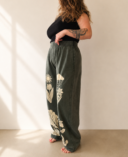 Person wearing green pants with floral designs in a minimal indoor setting
