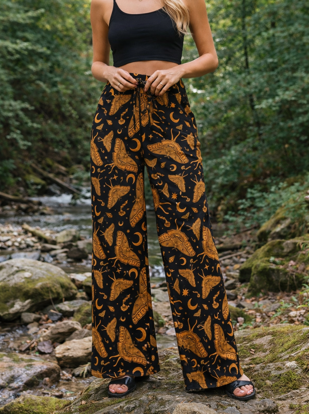 Woman wearing celestial luna moth patterned pants and black top in a forest setting