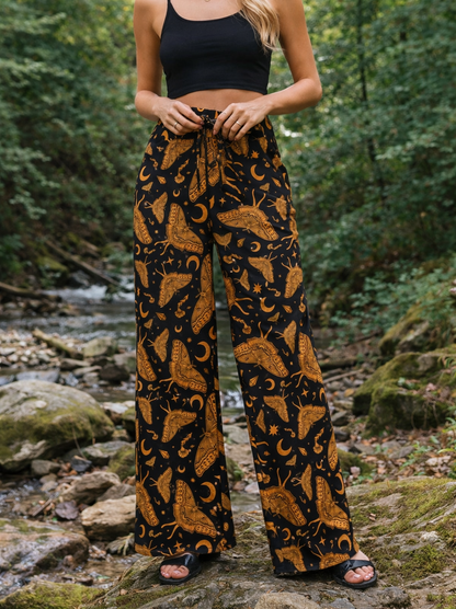Woman wearing celestial luna moth patterned pants and black top in a forest setting