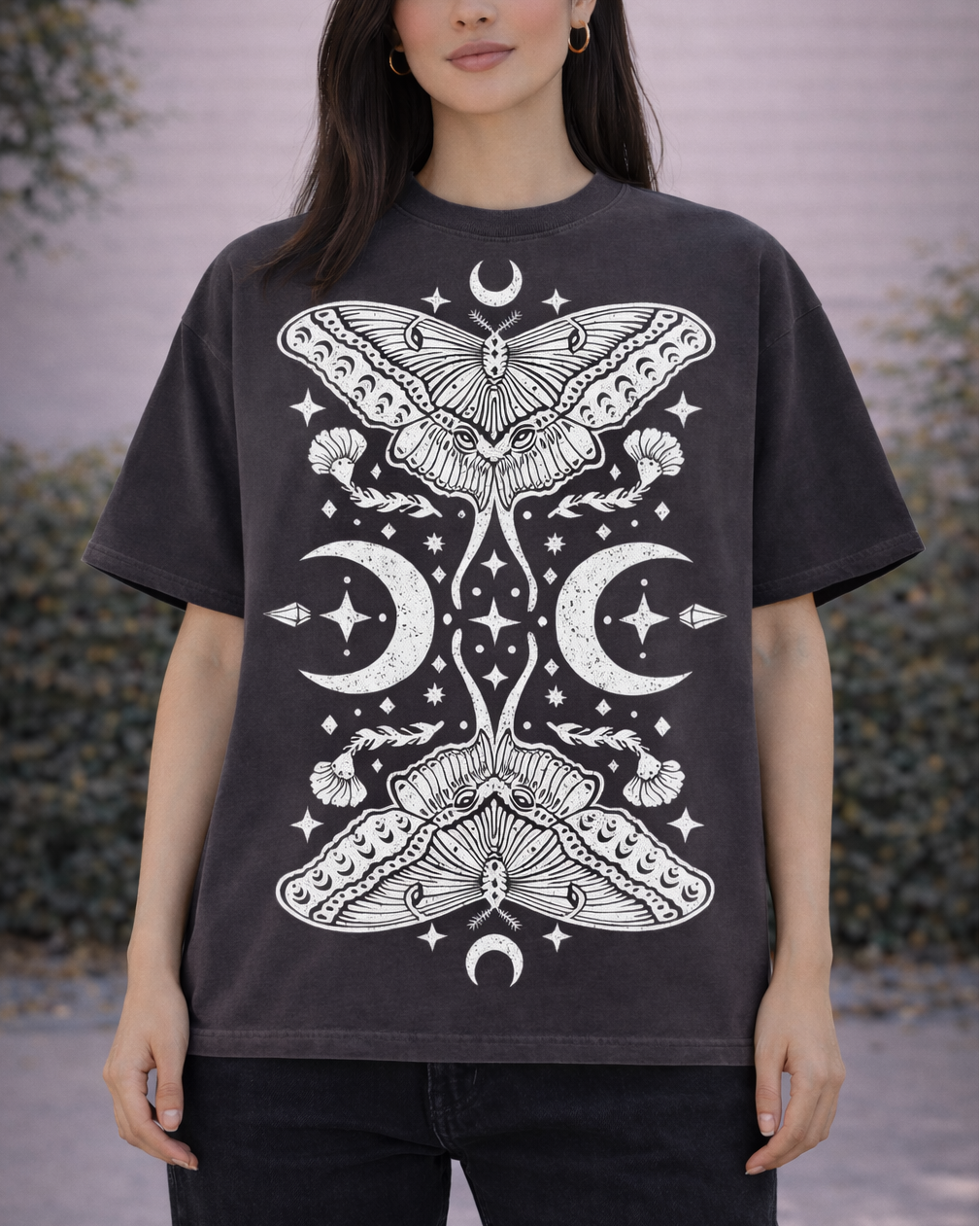 Person wearing a black t-shirt with white moth and celestial design outdoors.