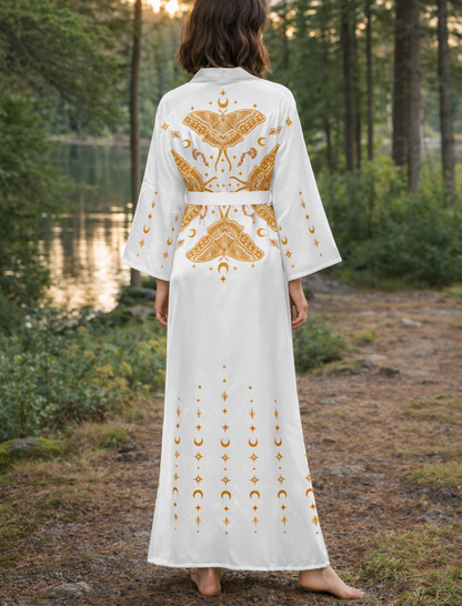 Woman in a white kimono robe dress with gold moth patterns standing in a forest by a lake.