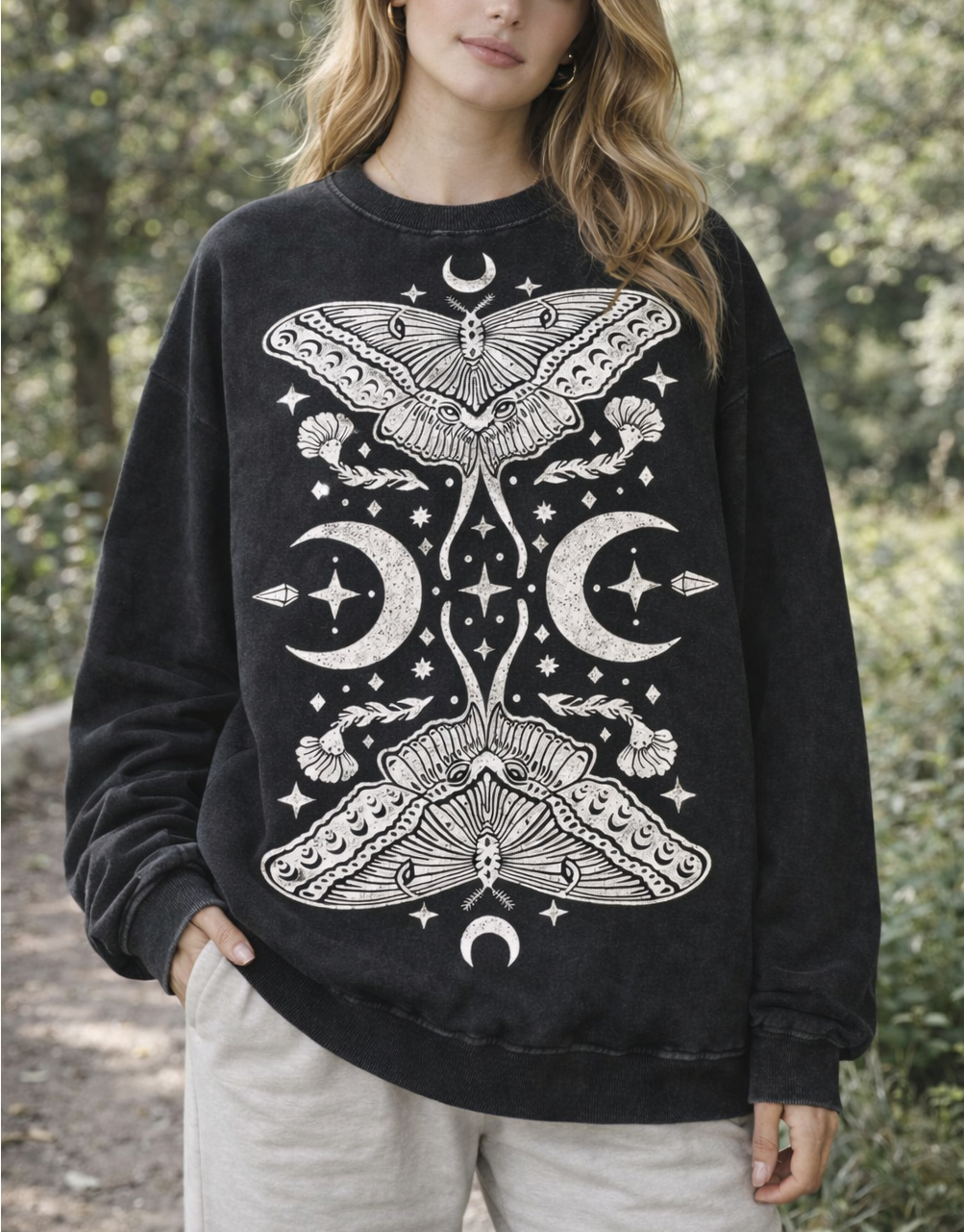 Woman wearing a black sweatshirt with white moth and moon design outdoors.
