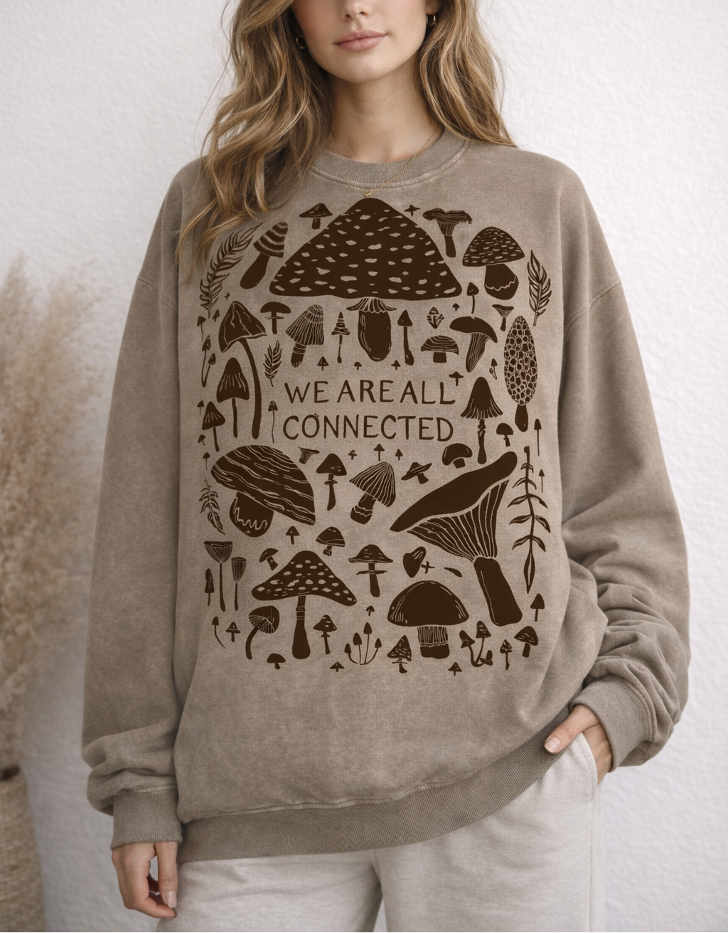 Woman wearing a beige sweatshirt with mushroom design and text.