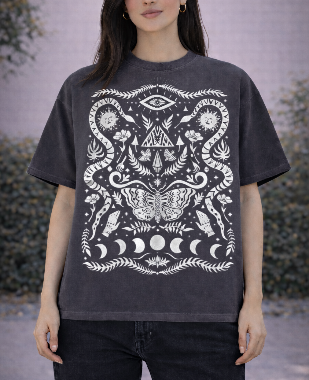 Person wearing a black mystical witchy pattern t-shirt with white graphic design outdoors