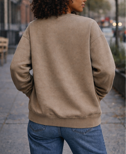 Person wearing a beige jacket and blue jeans walking on a city street.