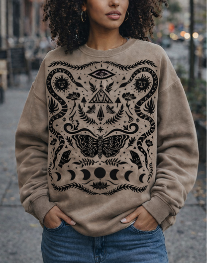 Woman wearing a beige sweatshirt with black intricate mystical witchy patterns in an urban setting