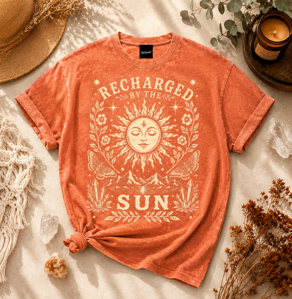 Orange t-shirt with sun graphic and 'Recharged by the Sun' text on a neutral background