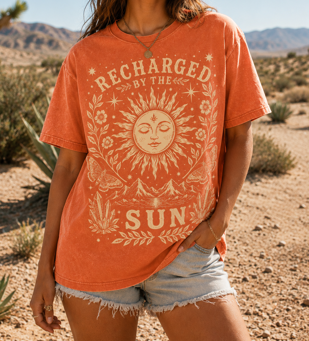 Woman wearing an orange t-shirt with a sun design and 'Recharged by the Sun' text in a desert setting.