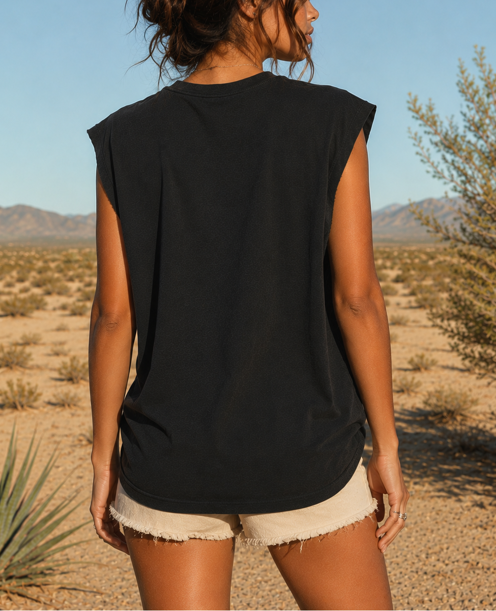 Woman wearing a black sleeveless top and beige shorts standing in a desert landscape.