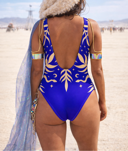 Person wearing a blue slimming snake and plant swimsuit with gold patterns in a desert setting