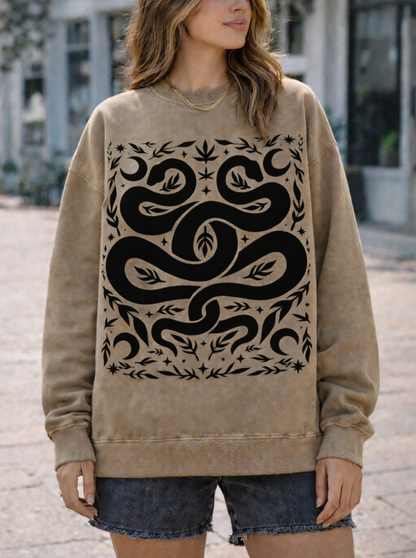 Woman wearing a beige sweatshirt with a black witchy snake design outdoors.