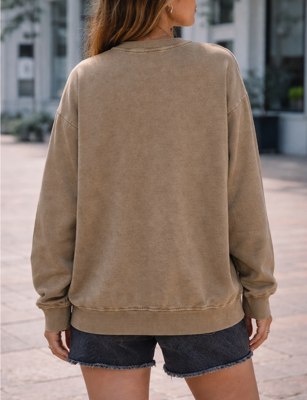 Person wearing a beige sweatshirt and denim shorts on a street.