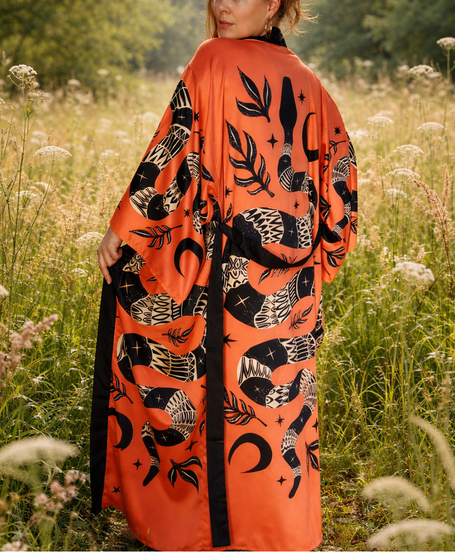 Woman wearing an ornamental snake orange kimono with black patterns in a field of tall grass and wildflowers.