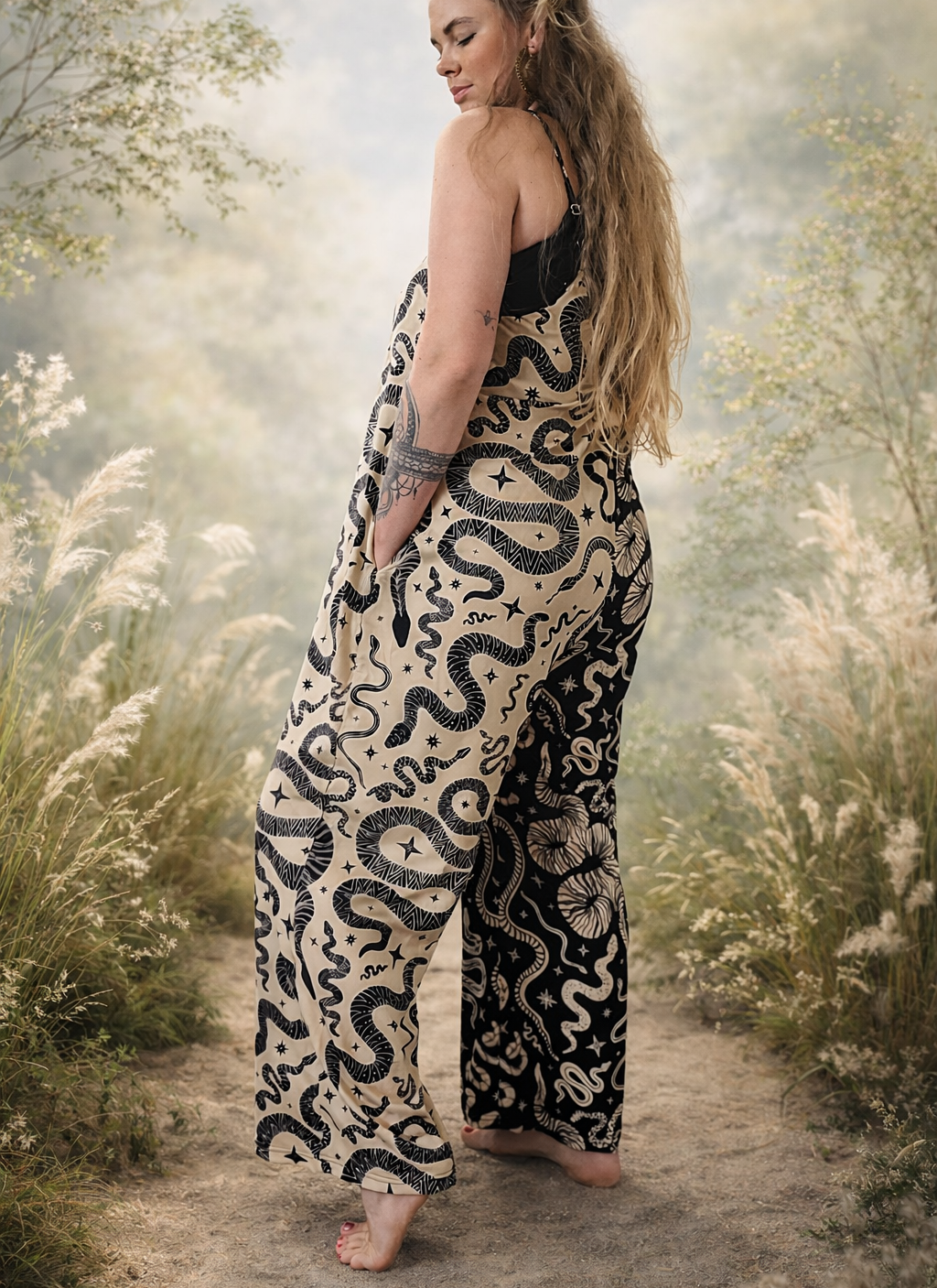 Woman wearing a snake-patterned color block loose jumpsuit stnding in a natural setting with trees and flowers