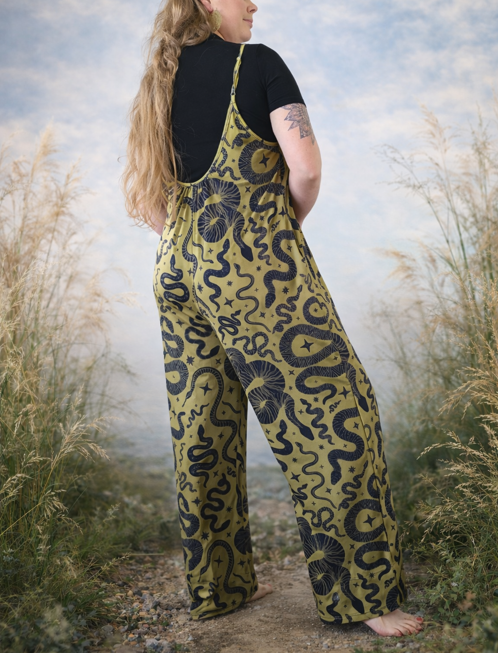 Person wearing a green snake patterned jumpsuit standing in a natural setting with grass and sky.